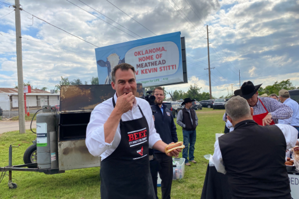 Oklahoma Gov. Kevin Stitt takes a bite of freshly grilled steak Wednesday in front of a PETA billboard the group purchased in response to the Governor’s vocal support of Oklahoma meat producers.