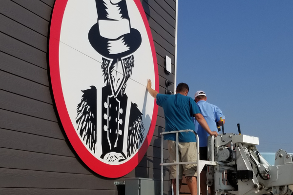 Workers attach the Slim Chickens bluesman logo sign to a side of the restaurant chain’s new Lawton location at 6731 NW Cache Road. ANDREW W. GRIFFIN/LEDGER PHOTOS