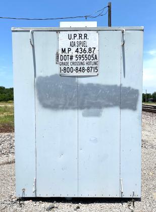 A grade crossing “hotline” number, and the unique identification number of the Union Pacific Railroad crossing on E. Ada Sipuel Ave. and Henderson St. in Chickasha, are posted on this nearby signal shed. MIKE W. RAY | SOUTHWEST LEDGER