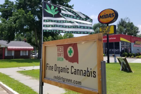 Southwest Ledger photo by Debi DeSilver        Red Dirt Green Dispensary, located at 2118 W. Lindsey St., in Norman, is nestled in among other businesses in a packed business district. A marijuana flag flies on a windy Oklahoma day, alerting potential customers of the medical marijuana location.