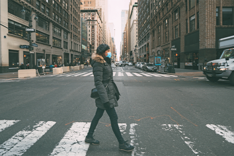 A woman wearing a surgical mask crosses a street in New York City’s midtown Manhattan.