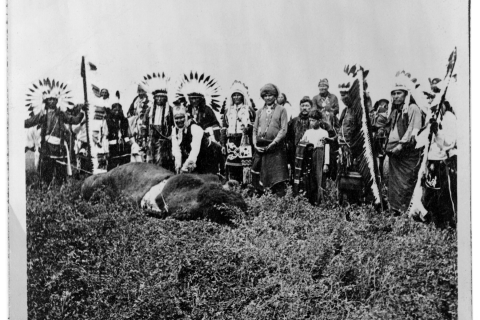 Geronimo stands over a dead buffalo, surrounded by indigenous men and boys in ceremonial dress in Fort Sill, circa 1906.