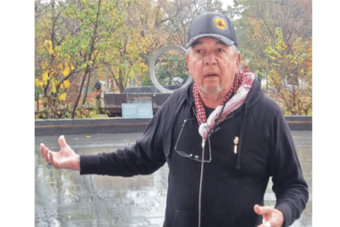 Harvey Pratt, designer of the National Native American Veteran Memorial, speaks with reporters Nov 11 at the Smithsonian national Museum of the American Indian in Washington, D.C. The memorial is seen behind Pratt. Photo By Jessie Christopher Smith, Gaylord News 