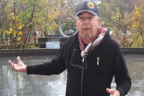 Harvey Pratt, designer of the National Native American Veteran Memorial, speaks with reporters on Nov. 11 at the Museum of the American Indian. The memorial can be seen in the distance over his shoulder. Jessie Christopher Smith/Gaylord News
