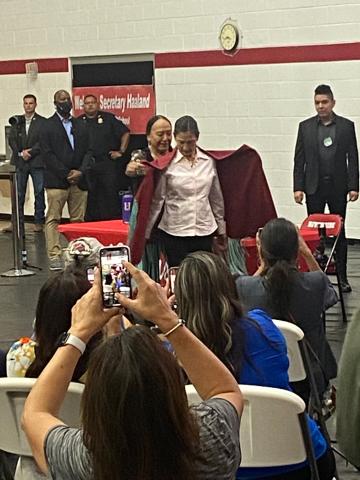 The audience watches as Delores Twohatchet, a Kiowa and Comanche woman, wraps a handmade shawl around Secretary of the Interior Deb Haaland July 11 at Riverside Indian School in Anadarko. Twohatchet and other survivors of the federal Indian boarding school system shared their stories during the first stop on the Interior Department’s “Road to Healing” tour.  Eric Swanson/Staff photo